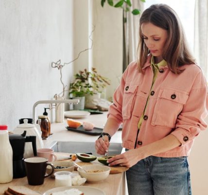 A woman slices an avocado in a bright, modern kitchen with natural light.