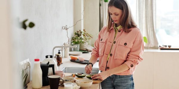 A woman slices an avocado in a bright, modern kitchen with natural light.