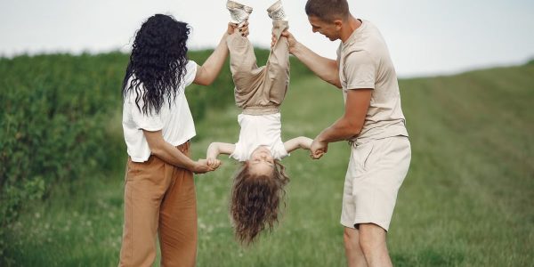 A joyful family enjoys outdoor play, lifting their child upside down in a green field.