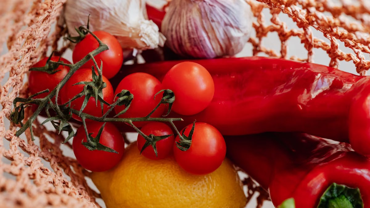 Top view of ripe tomatoes on branch arranged amidst fresh yellow lemon and red chili peppers with garlic in pink food net